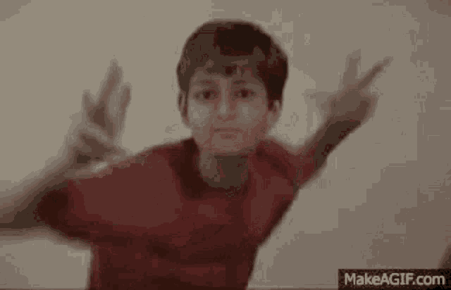 a boy in a red shirt is jumping in the air with his arms outstretched .