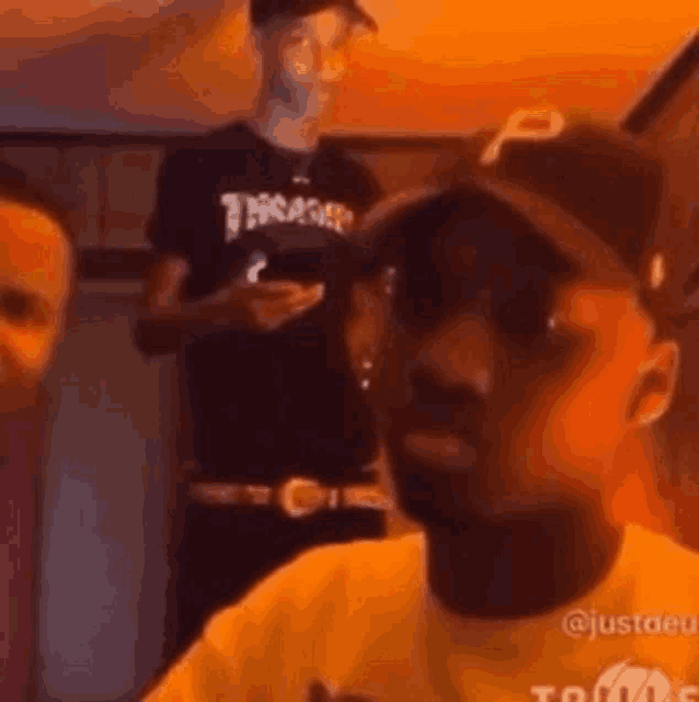 a man wearing a hat and a thrasher shirt is sitting in a room with other men .