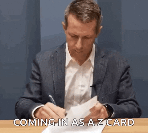 a man in a suit is sitting at a table writing on a piece of paper with the words coming in as a z card .