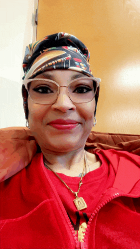 a woman wearing glasses and a red shirt has a necklace with the letter a on it