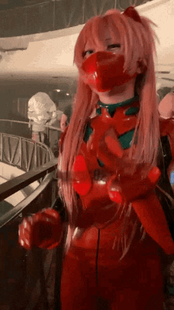 a woman with pink hair and a mask on her face is wearing a red suit