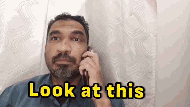 a man talking on a cell phone with the words look at this on the bottom