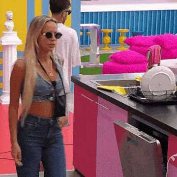 a woman wearing sunglasses stands in a kitchen next to a sink