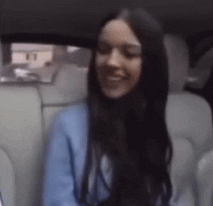 a woman with long black hair is sitting in the back seat of a car and smiling .