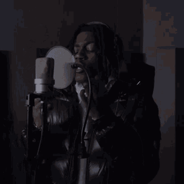 a man in a black jacket is standing in front of a microphone with his hand up