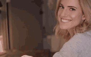 a woman in a grey sweater is smiling and looking over her shoulder