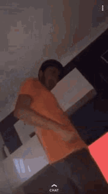 a man in an orange shirt is standing in a room holding a white box .