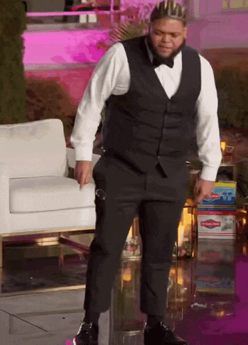 a man in a tuxedo with a crown on his head is standing next to a white chair