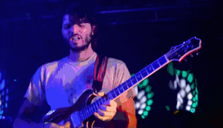 a man is playing a guitar in a dark room with red lights behind him
