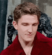 a young man in a red shirt is sitting in a chair with his eyes closed and smiling .