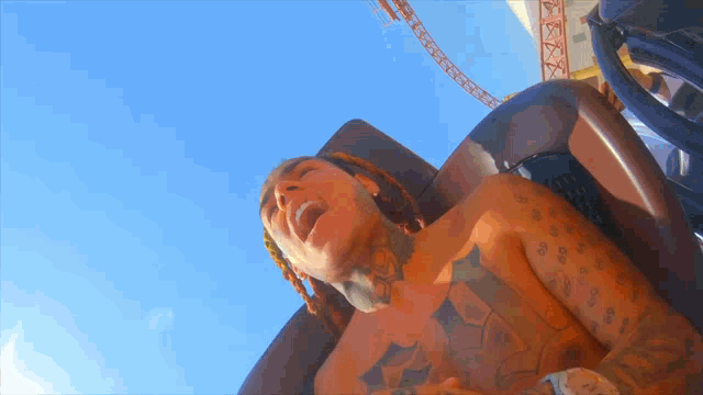 a shirtless man is riding a roller coaster with a blue sky in the background