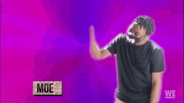 a man wearing a mask and a black shirt is dancing in front of a purple background with moe written on it .