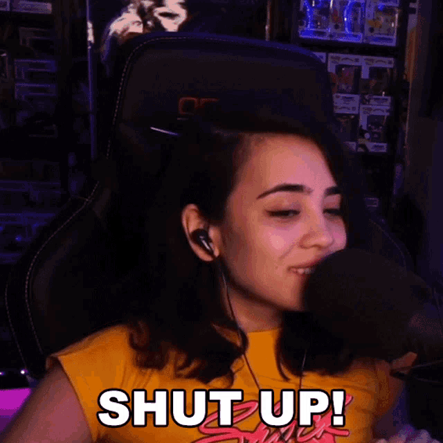 a woman in a yellow shirt is sitting in front of a microphone and saying shut up