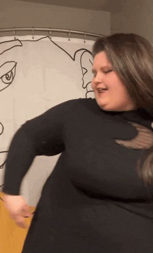 a woman in a black shirt is standing in front of a shower curtain with a drawing of a face on it .