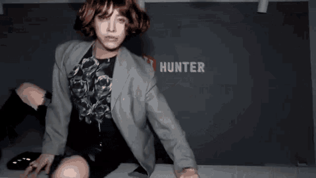 a woman in a suit and wig is sitting on a table in front of a hunter sign .