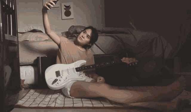 a woman laying on the floor with a guitar and taking a selfie