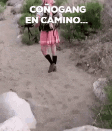 a woman in a pink skirt is walking down a dirt path holding a gun .