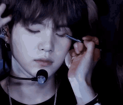 a close up of a person applying eyeliner to a young man 's eye .