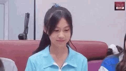 a girl in a blue shirt is sitting on a red couch and smiling .