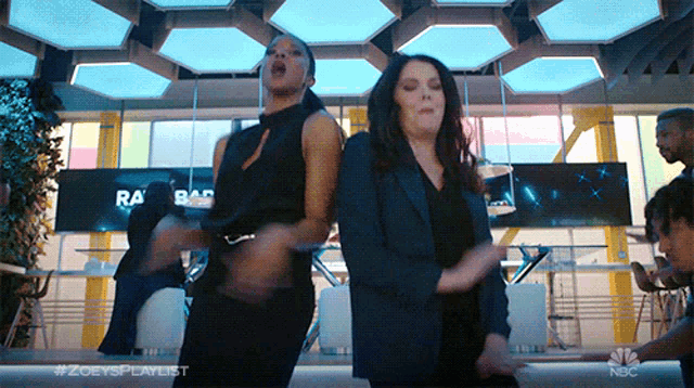 two women are dancing in front of a sign that says nbc on it