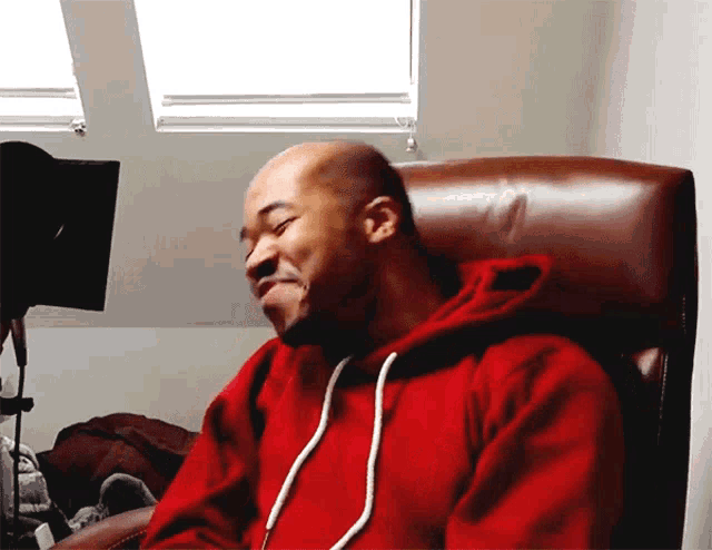 a man in a red hoodie sits in a leather chair