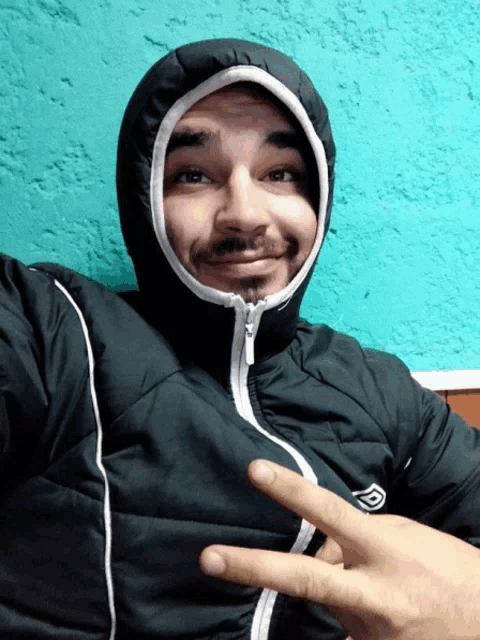 a man wearing a jacket with a hood on his head is giving the peace sign