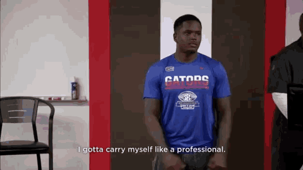 a man wearing a blue gators shirt is standing in a room .