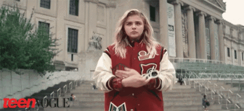 a girl wearing a red and white varsity jacket is standing in front of a building