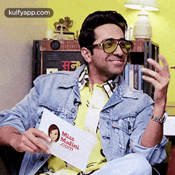 a man wearing sunglasses and a denim jacket is sitting in a chair holding a piece of paper .