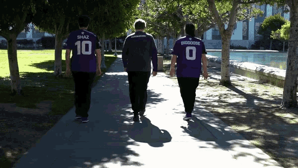 three people are walking down a sidewalk wearing purple shirts with the number 10 on the back
