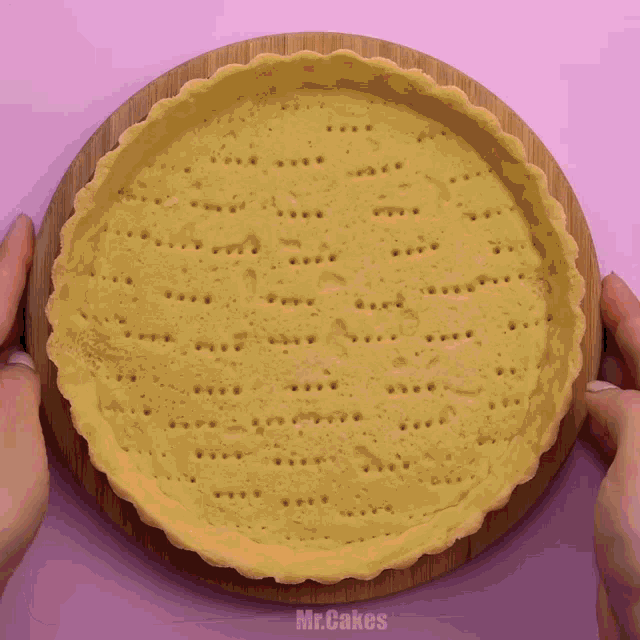 a person is holding a pie crust on a wooden cutting board with the words mr.cakes on the bottom