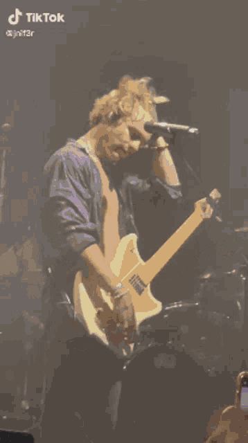 a man without a shirt is playing a guitar and singing into a microphone