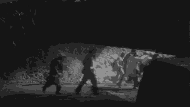 a black and white photo of a group of men walking in the dark .
