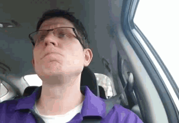 a man in a purple shirt and glasses is sitting in a car