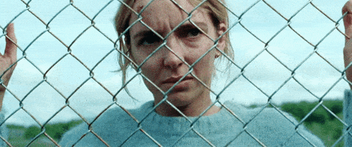 a woman looking through a chain link fence with a serious look on her face