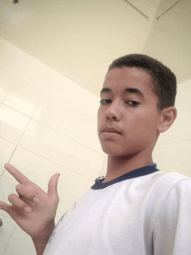 a boy wearing a white shirt with a blue collar points to the camera