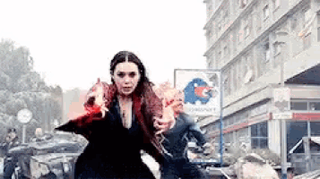 a woman in a red cape is walking down a street in front of a large building .