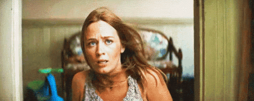 a woman is standing in a doorway holding a mop and looking scared .