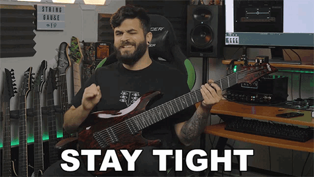 a man playing a guitar in front of a sign that says " stay tight "