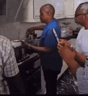 a group of men are standing in a kitchen preparing food while one man is holding a cell phone .