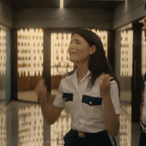 a woman in a white shirt and black pants stands in a hallway with her eyes closed