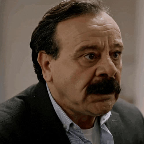 a man with a mustache is wearing a suit and blue striped shirt