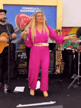 a woman in a pink jumpsuit is singing on stage