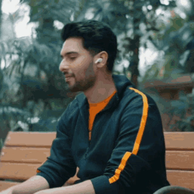 a man wearing ear buds sits on a park bench