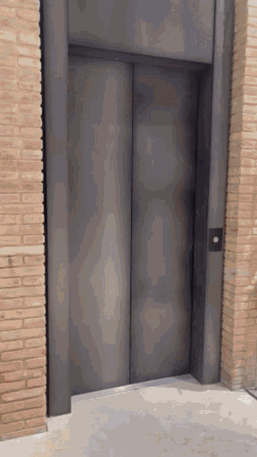 a gray elevator with a brick wall in the background