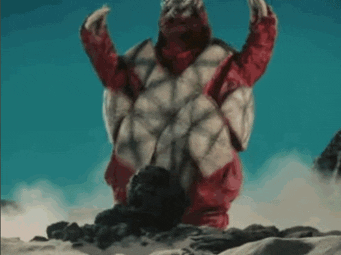 a red and white monster is standing on top of a rocky hill .