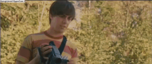 a man in a striped shirt is holding a camera in front of a bush with a hypercam 2 watermark
