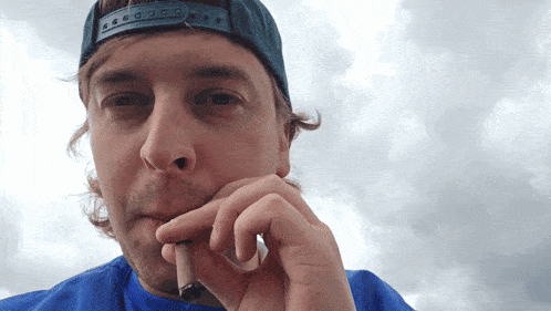 a man wearing a blue shirt and a black hat smoking a cigarette