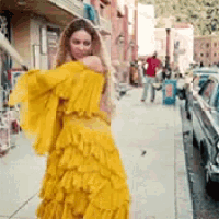 a woman in a yellow dress is standing on a sidewalk in a city .