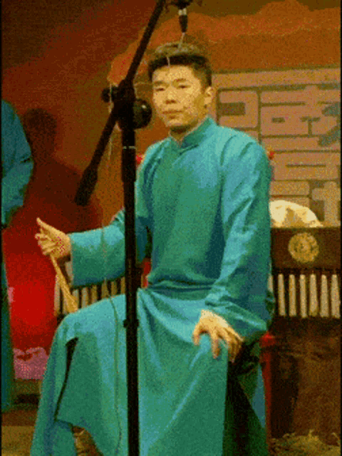 a man in a blue robe is sitting in front of a microphone and holding a stick